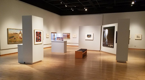 A spacious art gallery featuring various paintings and sculptures displayed on light-colored walls.