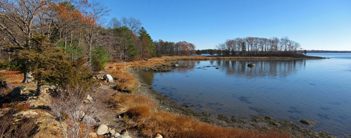 A serene landscape featuring a calm river, autumn foliage, and a distant island under a clear blue sky.