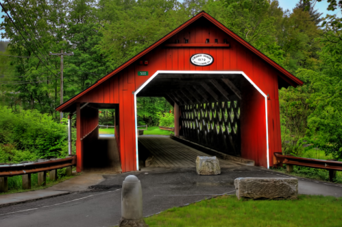 A red covered bridge surrounded by lush greenery, with a stone barrier and a clear path leading through it.