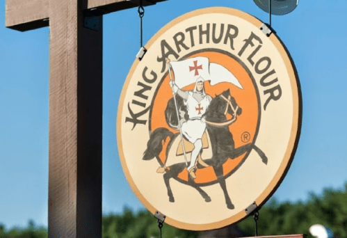 Sign for King Arthur Flour featuring a knight on horseback, with text indicating a bakery, café, store, and school.