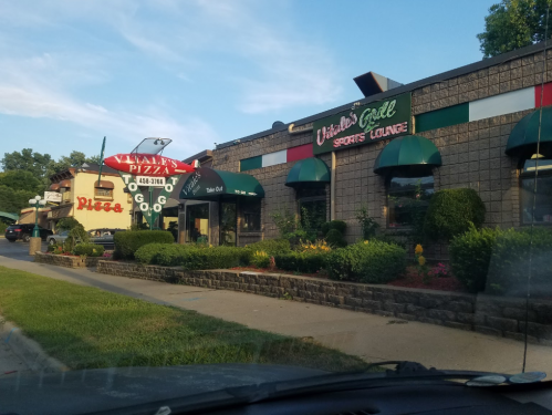 A view of a pizza restaurant and a sports lounge, featuring outdoor seating and green awnings on a sunny day.