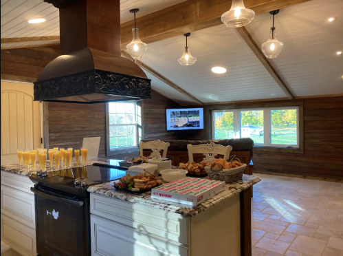 A spacious kitchen with a large island, featuring drinks and pastries, and a TV in a cozy, rustic setting.