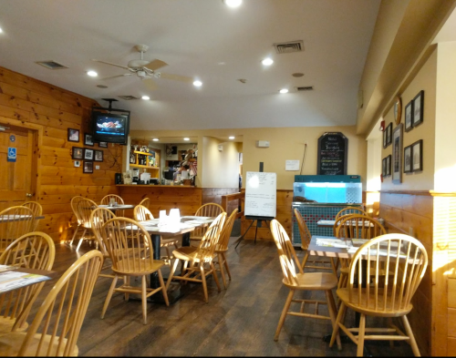 Cozy restaurant interior with wooden walls, tables, and chairs, featuring a bar area and a TV in the background.