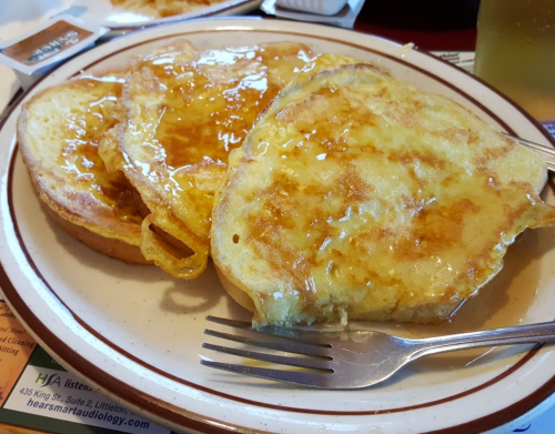 A plate of French toast drizzled with syrup, accompanied by a fork.