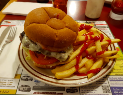 A juicy burger with lettuce, tomato, and cheese, served with a side of crispy fries and ketchup on a plate.