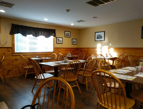 Cozy restaurant interior with wooden tables and chairs, sunlight streaming through a window, and framed photos on the walls.