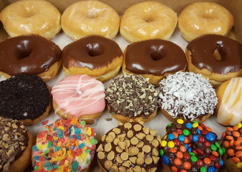 A box of assorted donuts, including glazed, chocolate, and various topped varieties with colorful sprinkles and candies.