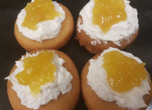 Four cupcakes topped with whipped cream and a dollop of yellow fruit preserves.
