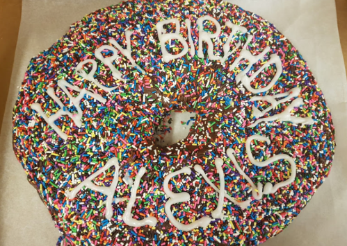 A large donut covered in colorful sprinkles with "Happy Birthday Alexis" written in white icing.