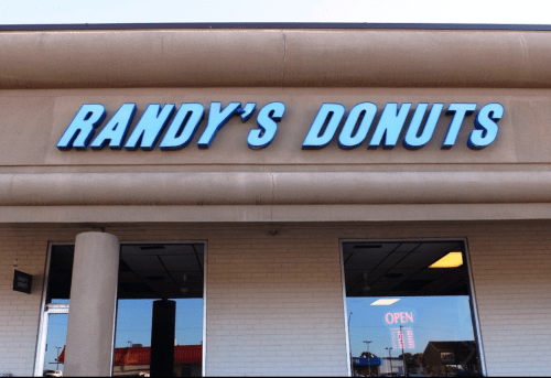 Sign for Randy's Donuts, featuring bold blue letters on a beige building, with an "OPEN" sign visible in the window.