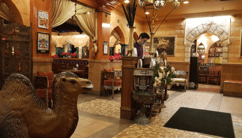 A cozy restaurant interior featuring a camel statue, ornate decor, and a staff member at the reception desk.