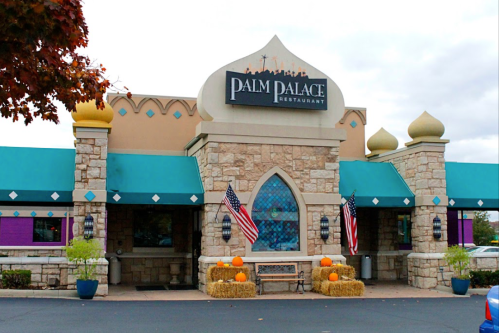 Exterior of Palm Palace Restaurant featuring stone architecture, colorful awnings, and autumn decorations with pumpkins.