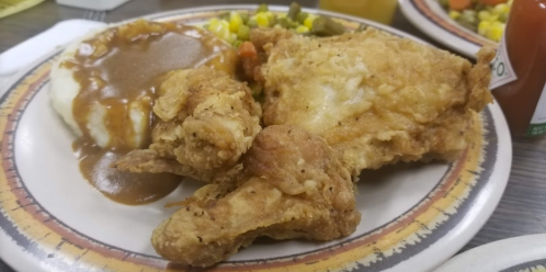 A plate of fried chicken with gravy, mashed potatoes, and mixed vegetables.