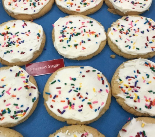 A close-up of frosted sugar cookies topped with colorful sprinkles on a blue surface.