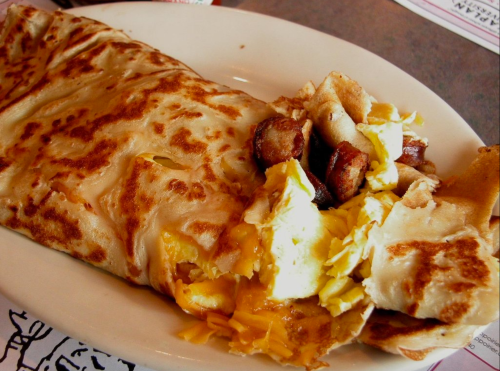 A plate featuring a golden-brown breakfast burrito with melted cheese and scrambled eggs, alongside crispy potatoes.