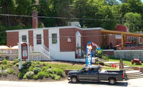 A brick building with a sign for ice cream, surrounded by greenery and a parked truck in front.