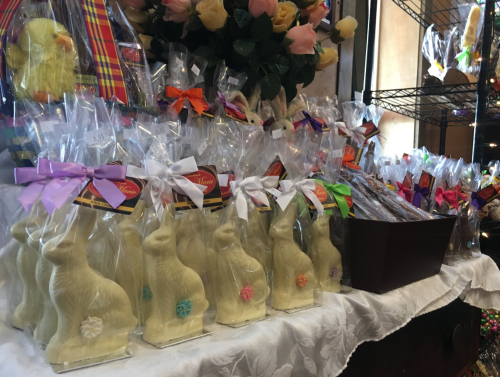 A display of chocolate bunnies wrapped in clear bags with colorful ribbons, surrounded by decorative flowers.