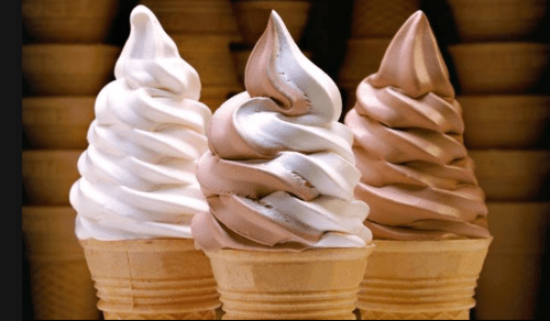 Three ice cream cones with swirled soft serve: vanilla, chocolate, and a mix of both, against a blurred background.