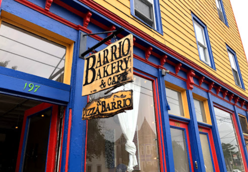 Sign for "Barrio Bakery & Café" hanging outside a colorful building with blue and yellow paint.