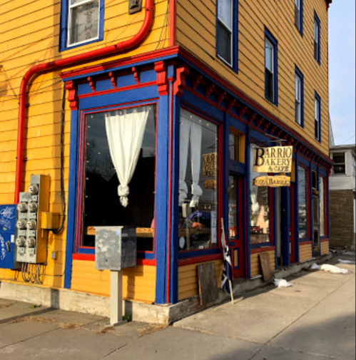Colorful bakery storefront with blue and yellow paint, large windows, and a sign reading "Barrio Bakery & Cafe."