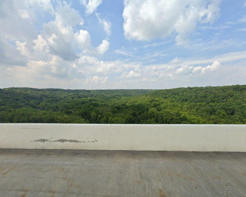 A scenic view of lush green hills under a partly cloudy sky, seen from a concrete barrier.