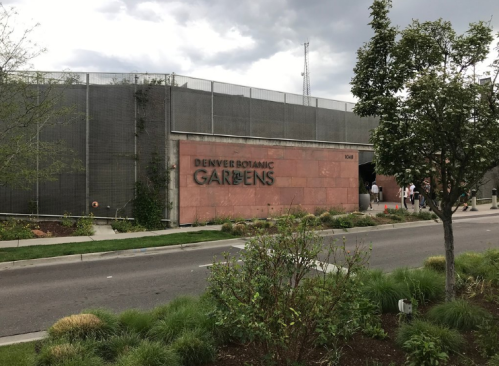 Entrance to the Denver Botanic Gardens, featuring a stone wall with the name displayed prominently. Greenery in the foreground.