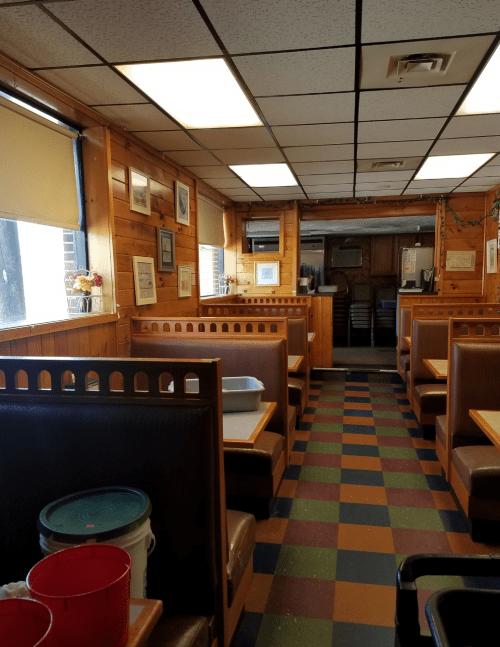Interior of a cozy diner with wooden paneling, booths, and a colorful tiled floor. Buckets are visible in the foreground.