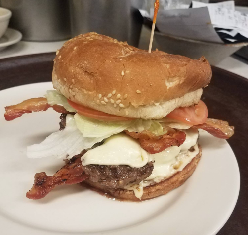 A juicy burger with melted cheese, bacon, lettuce, and tomato, served on a sesame seed bun with a toothpick.