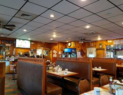 Interior of a cozy diner with wooden paneling, booths, and a TV, featuring tables set for dining.