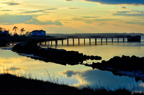 A serene sunset over a calm waterway, with a pier and a house silhouetted against the colorful sky.