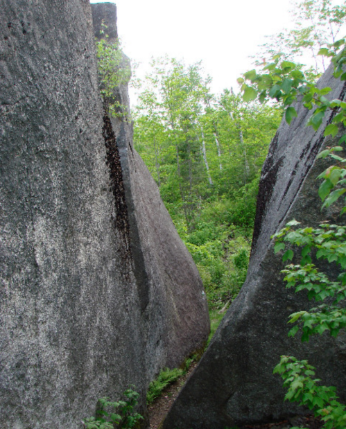 Narrow passage between large rocks, surrounded by lush green trees and foliage.