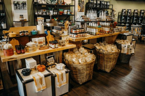 A cozy store display featuring shelves of jars, bottles, and baskets filled with various gourmet food products.