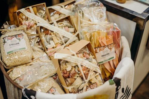 A basket filled with various types of packaged pasta and grains, beautifully arranged with decorative labels.