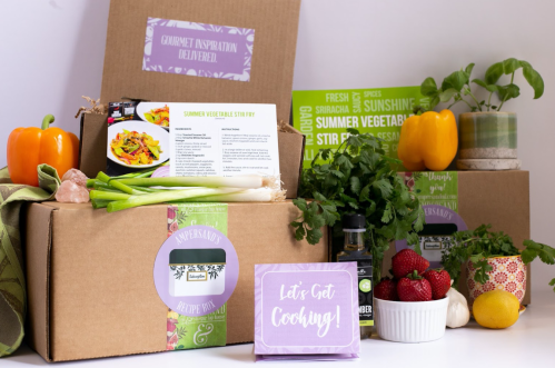A collection of meal kit boxes with fresh vegetables, herbs, and a recipe card for summer vegetable stir fry.