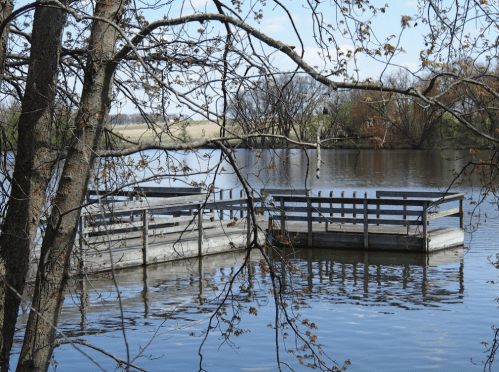 A serene lake scene featuring wooden docks surrounded by trees and calm water under a clear blue sky.