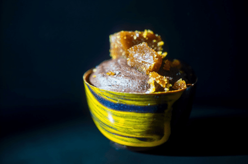 A dark, creamy dessert topped with golden, crystalline sugar in a colorful bowl against a dark background.