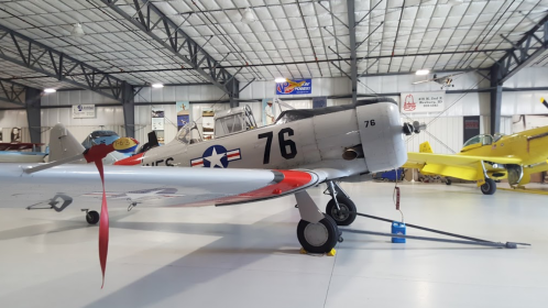 A vintage aircraft with military markings, parked inside a hangar alongside other planes.