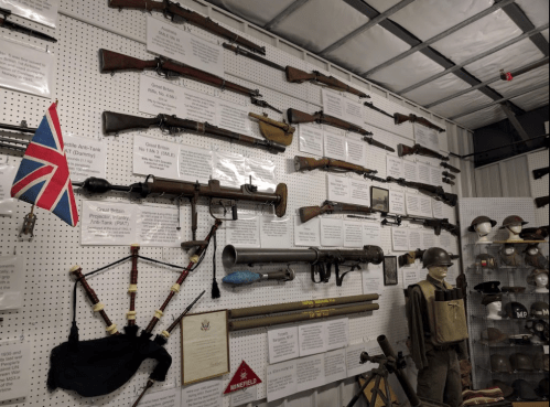 A display of various historical firearms and military artifacts on a wall, with informational plaques and a British flag.