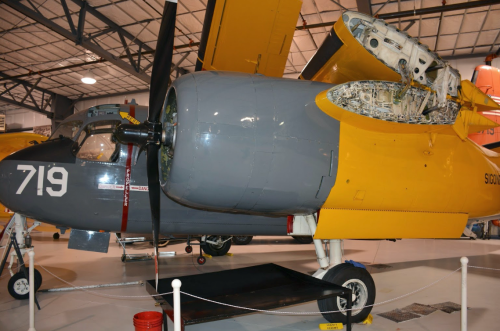 A vintage aircraft with a gray and yellow exterior, showcasing its engine and propeller in a hangar setting.