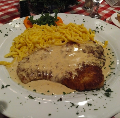 A plate of breaded chicken covered in creamy sauce, served with yellow noodles and garnished with parsley and orange slices.