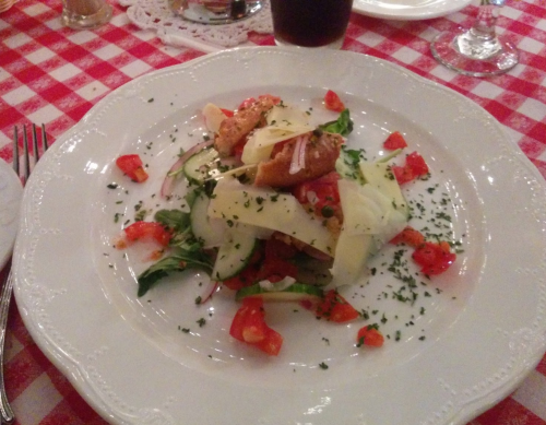 A plate of salad with greens, tomatoes, cheese, and crispy elements, served on a checkered tablecloth.