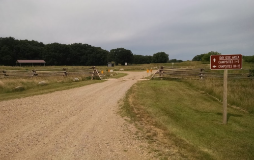 A gravel road leads to a campsite area, with a sign indicating directions to day use and campsites.