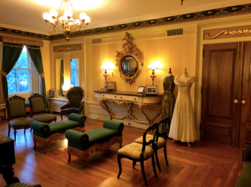 Elegant vintage room with yellow walls, antique furniture, a dress form, and soft lighting.