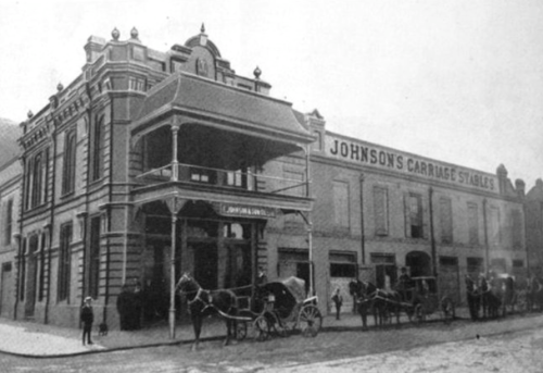Historic black-and-white photo of Johnson's Carriage Stables, featuring horse-drawn carriages and a two-story building.