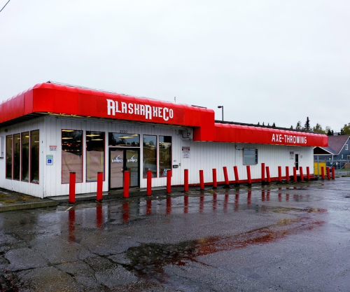 Axe-throwing venue with a red roof and signage, located in a rainy, overcast setting.