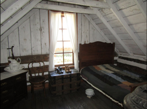 Cozy attic room with a bed, wooden furniture, a window, and vintage decor.