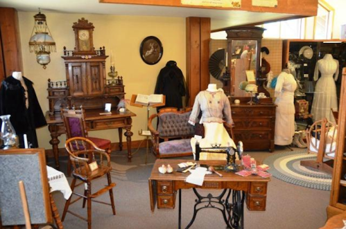 A vintage display featuring antique furniture, clothing, and decor in a museum setting.