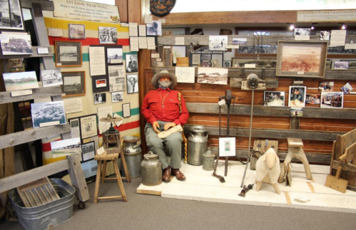 A museum display featuring a seated mannequin in red attire, surrounded by historical photos and artifacts.