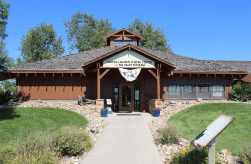 A wooden visitor center with a sloped roof, surrounded by grass and trees, featuring a sign for a museum.