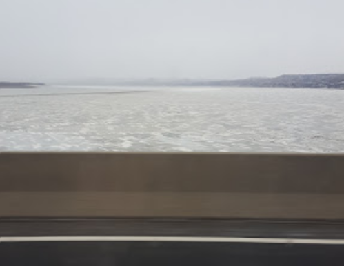 A view of a wide river with icy water, seen from a bridge on a cloudy day.